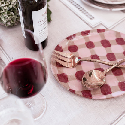 Wine bottle, glass, and checkered plate with cutlery on a table setting.
